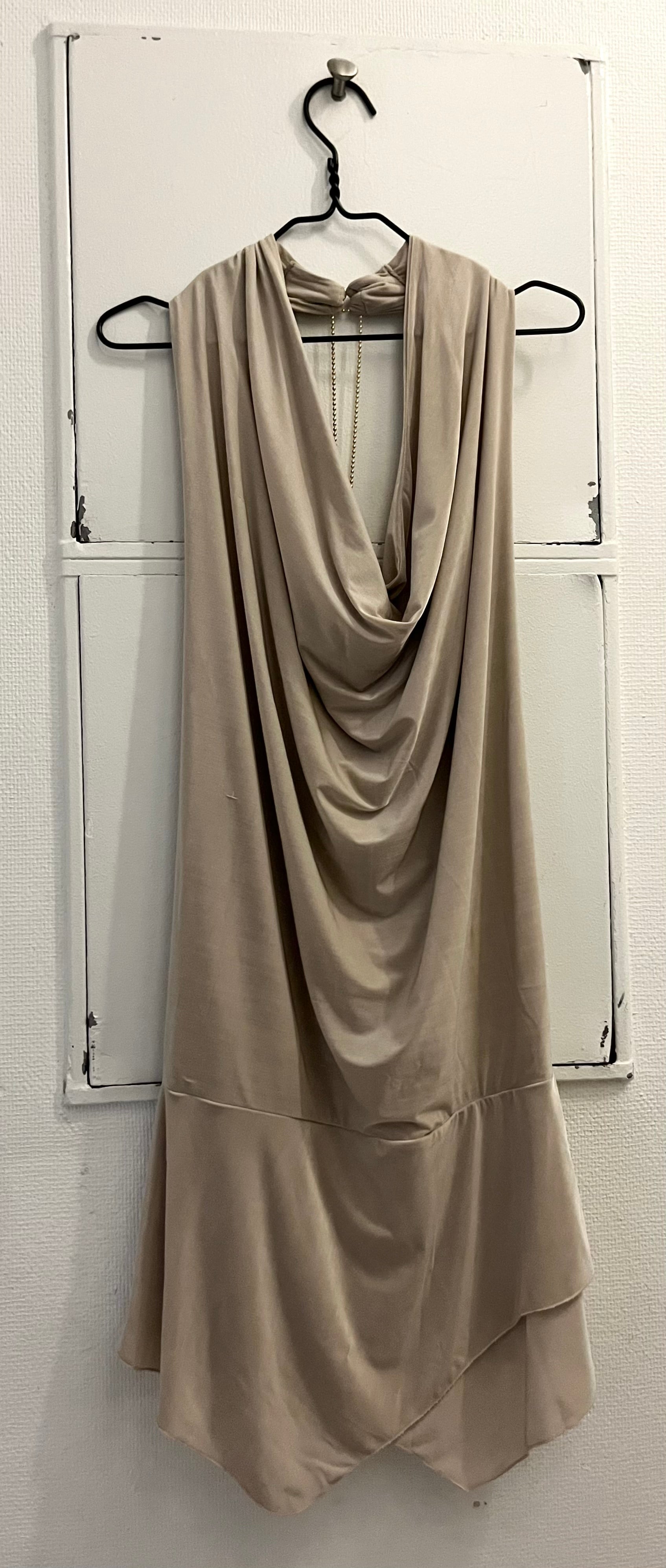 Elegant beige backless kjole i strækbar jersey materiale med med åben ryg og draperet halsudskæring – perfekt til festlige anledninger og tidløse looks
